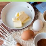 bowl of butter, eggs, flour on table with a whisk